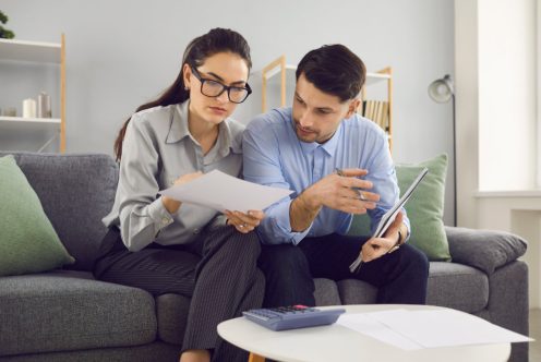 Family budget planning. Married couple analyzes and calculates their financial accounts while sitting on the couch. Family plans expenses and purchases or calculates payment for utilities and rent.